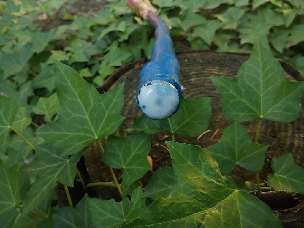 Tip of broom handle capped with a moss agate cabochon style stone, nestled among green ivy leaves outdoors.